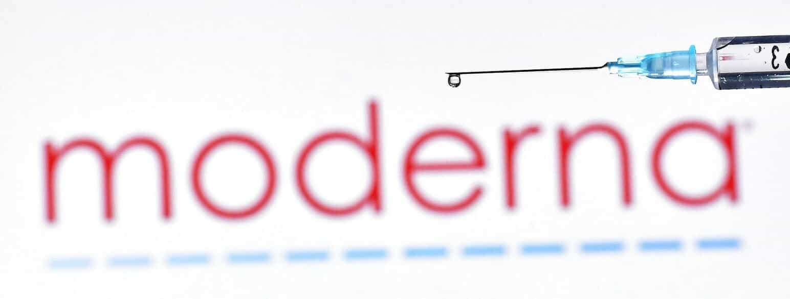En fyldt injektionssprøjte foran Moderna Inc.'s logo