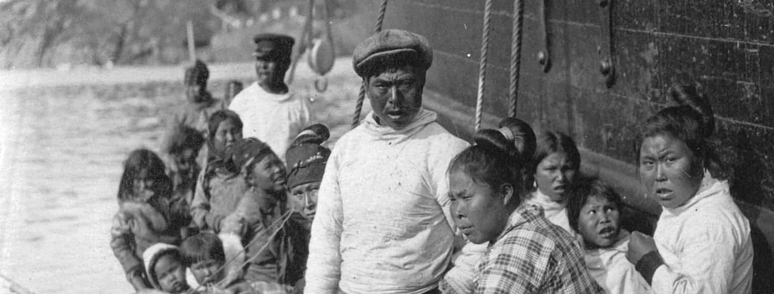 En gruppe mennesker i umiaq har lagt til et skib, antageligt ved den østgrønlandske koloni Ammassalik (i dag Tasiilaq) omkring år 1924