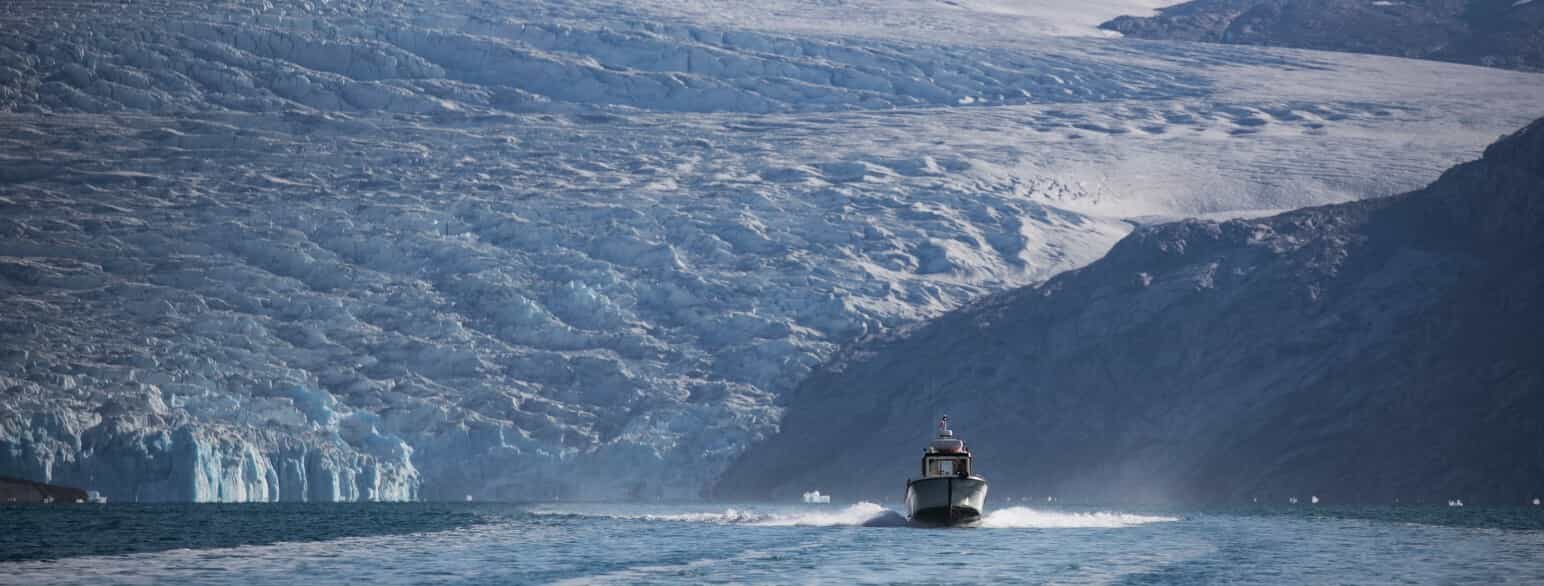 En båd stævner ud af den lange, snoede Kangerlussuatsiaq (Evighedsfjorden) med de stejle fjeldsider og mange bræudløb