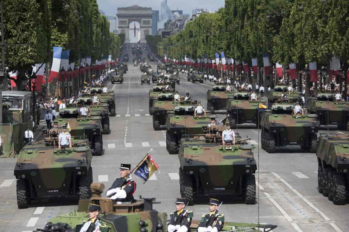 Kampvogne kører i parade på den brede Champs-Élysées. I baggrunden ses Triumfbuen.