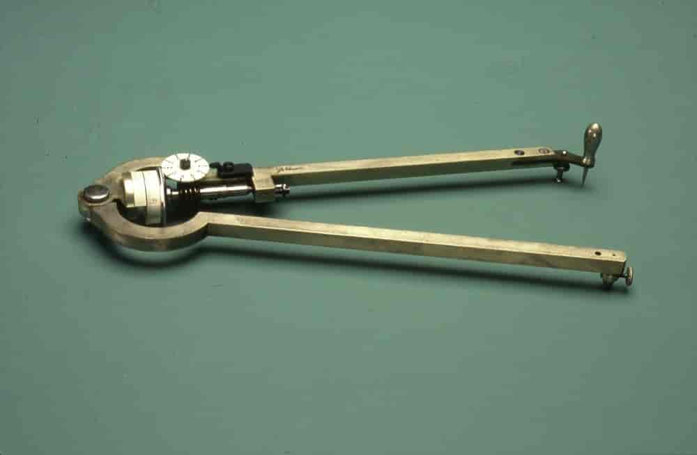 Passerlignende instrument i gulligt metal med to sammenhængslede arme.