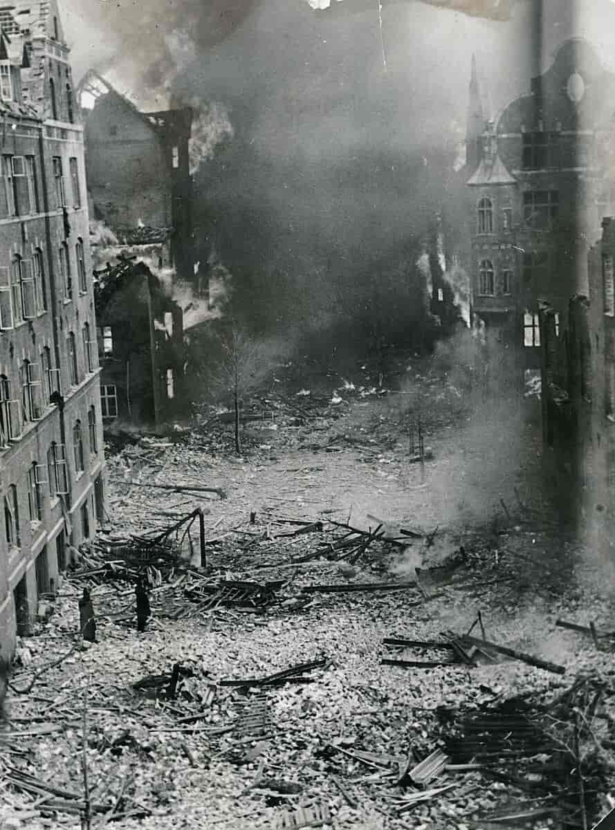 På billedet ser man udbombede bygninger, indhyllet i røg og flammer